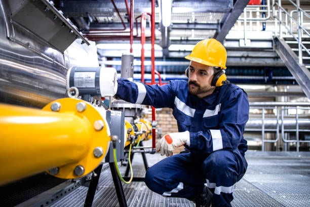 Technician in coveralls and ear protection checking an instrument on a plant line